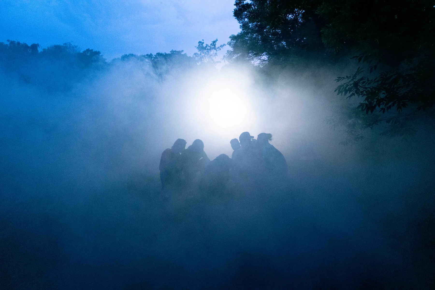 Figures silhouetted in blue fog under a single bright light at night.