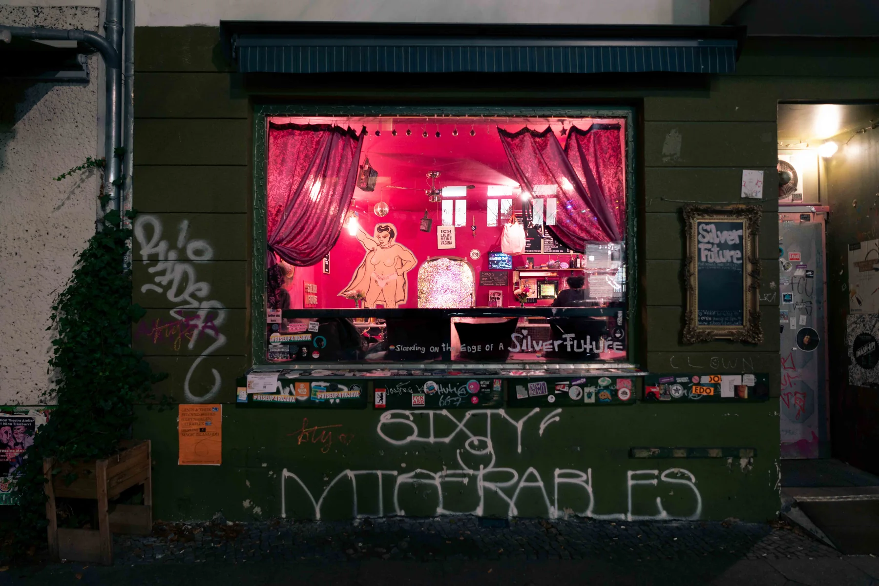A bar window lit red at night, graffiti spread across the facade around it.