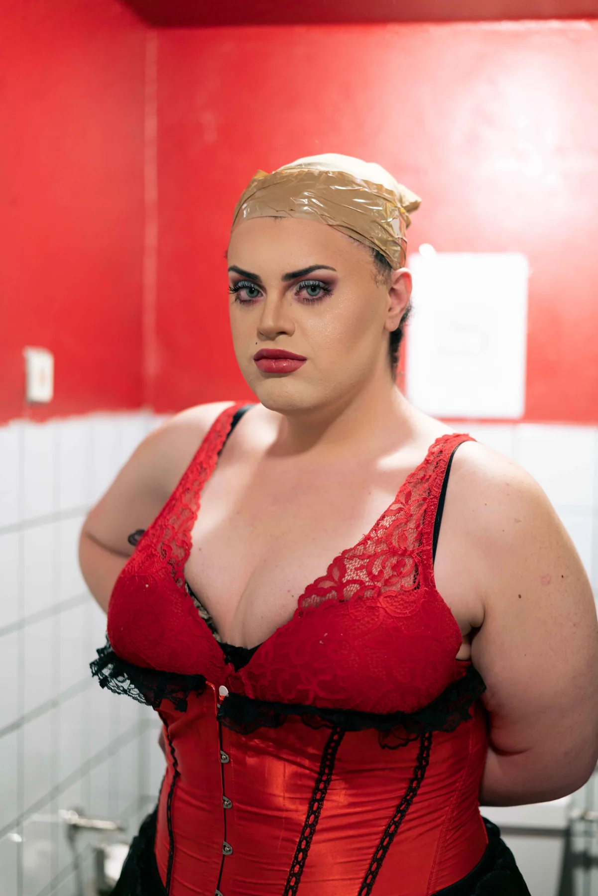 A portrait of a person in a red corset against a red wall.