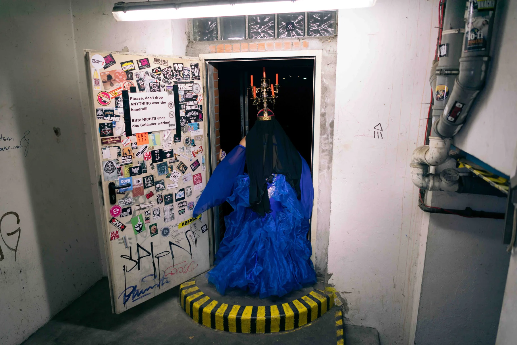 A figure in a blue gown stands in a basement doorway crowned by a lit candelabra.